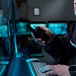 A male security guard for Royal Caribbean Cruises sits in a control room, looking at video footage of an onboard disruption, and calls for backup on his walkie-talkie.